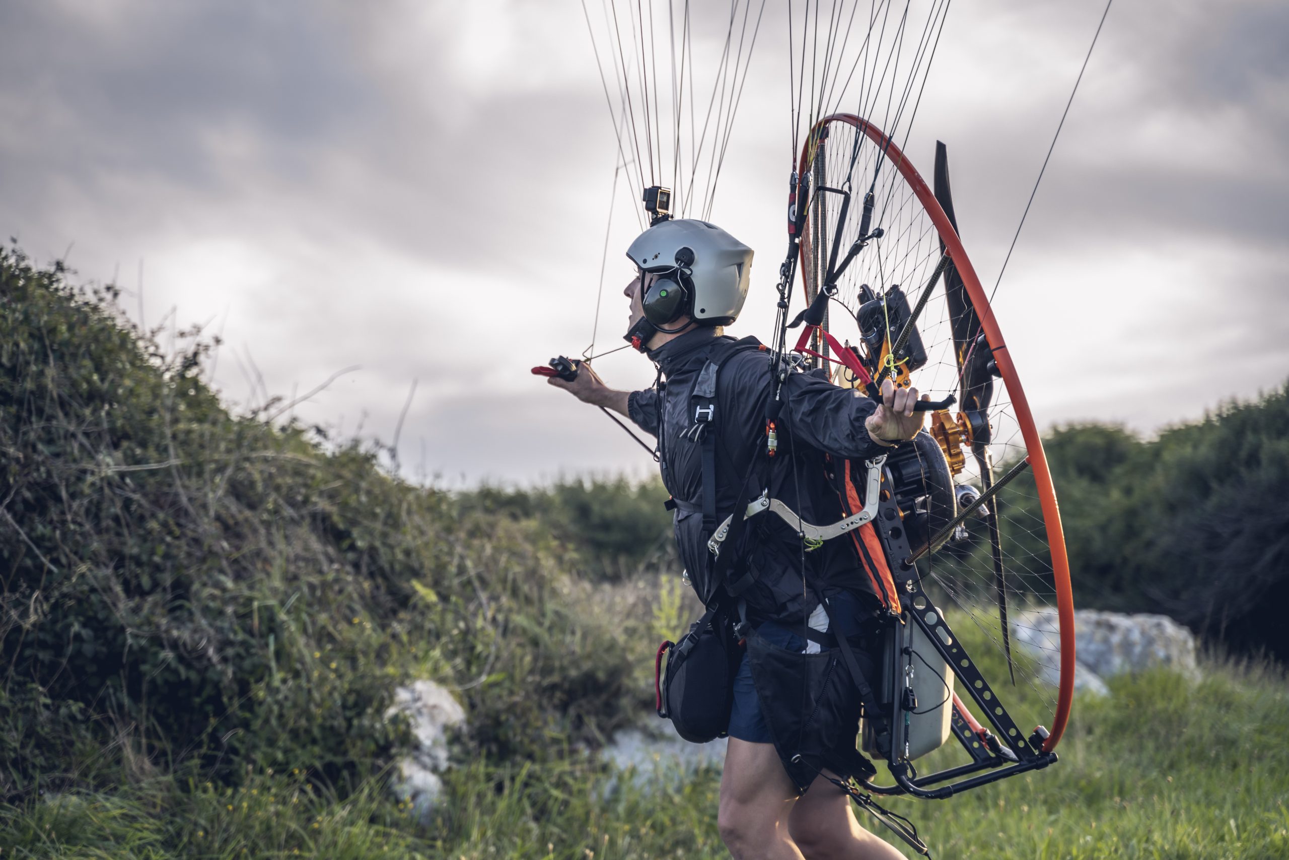 Young man, with the Powered Paragliding engine in his shoulders, runs on the lawn, and gets ready to jump and fly.